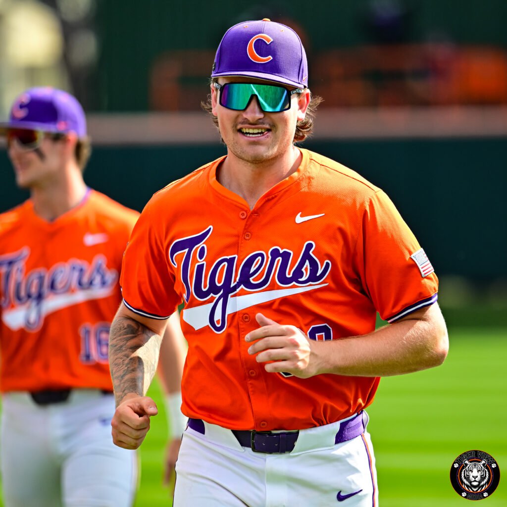 Collin Priest in orange uniform and sunglasses running on a field