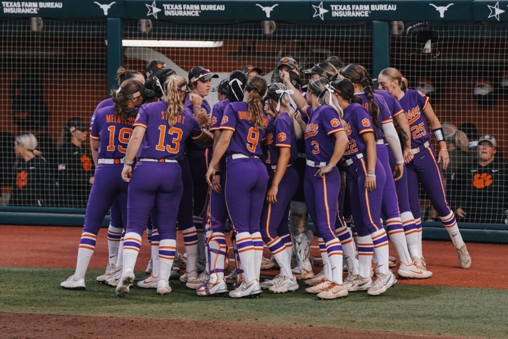 Clemson softball team gathers in a huddle wearing purple uniforms, showing team spirit during the Super Regional at Texas.